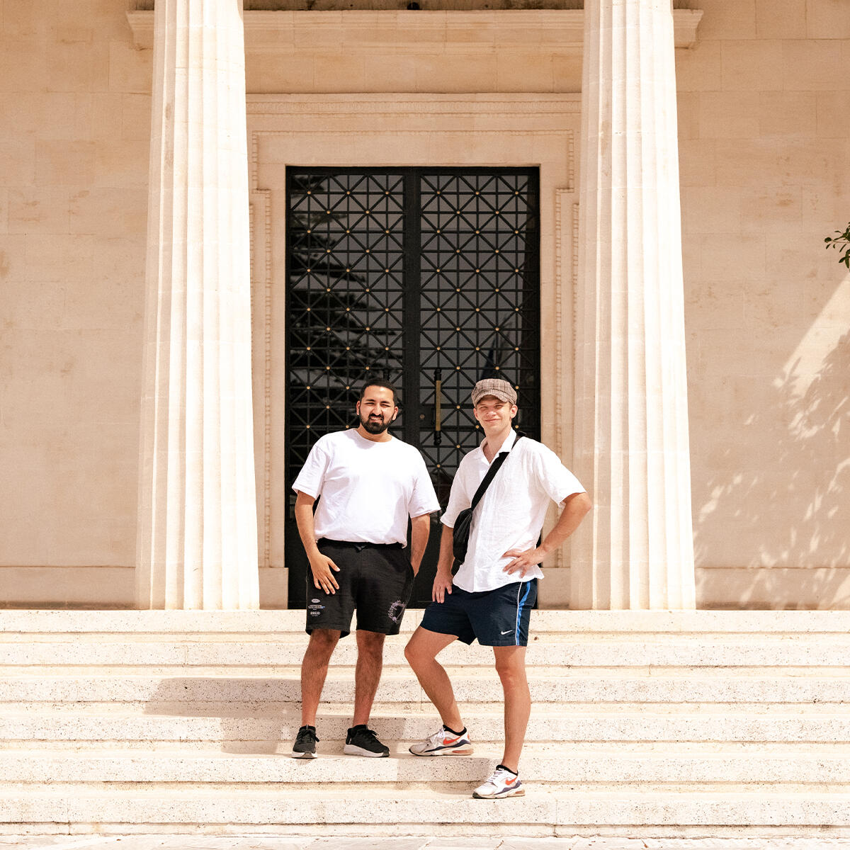 Leroy & Maziar Links steht Maziar, Rechts Leroy, beide stehen vor einem schicken Gebäude mit Säulen.